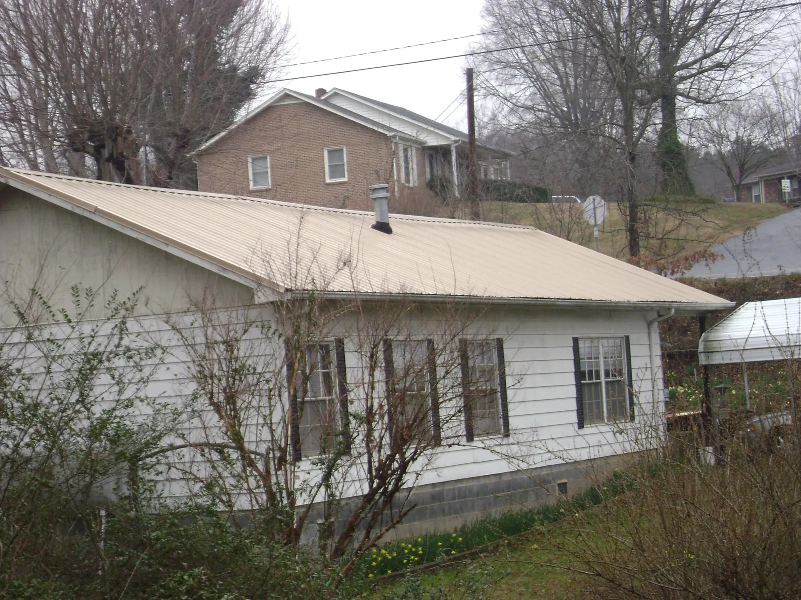 Tan metal roof on a white sided house set into a hillside — Commercial Roofing by Roofing Brothers in Rosebud